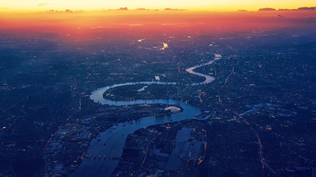 An aerial photo of the long and winding River Thames. It's dark over much of the river including Central London with sunlight at the top of the image in the distance.